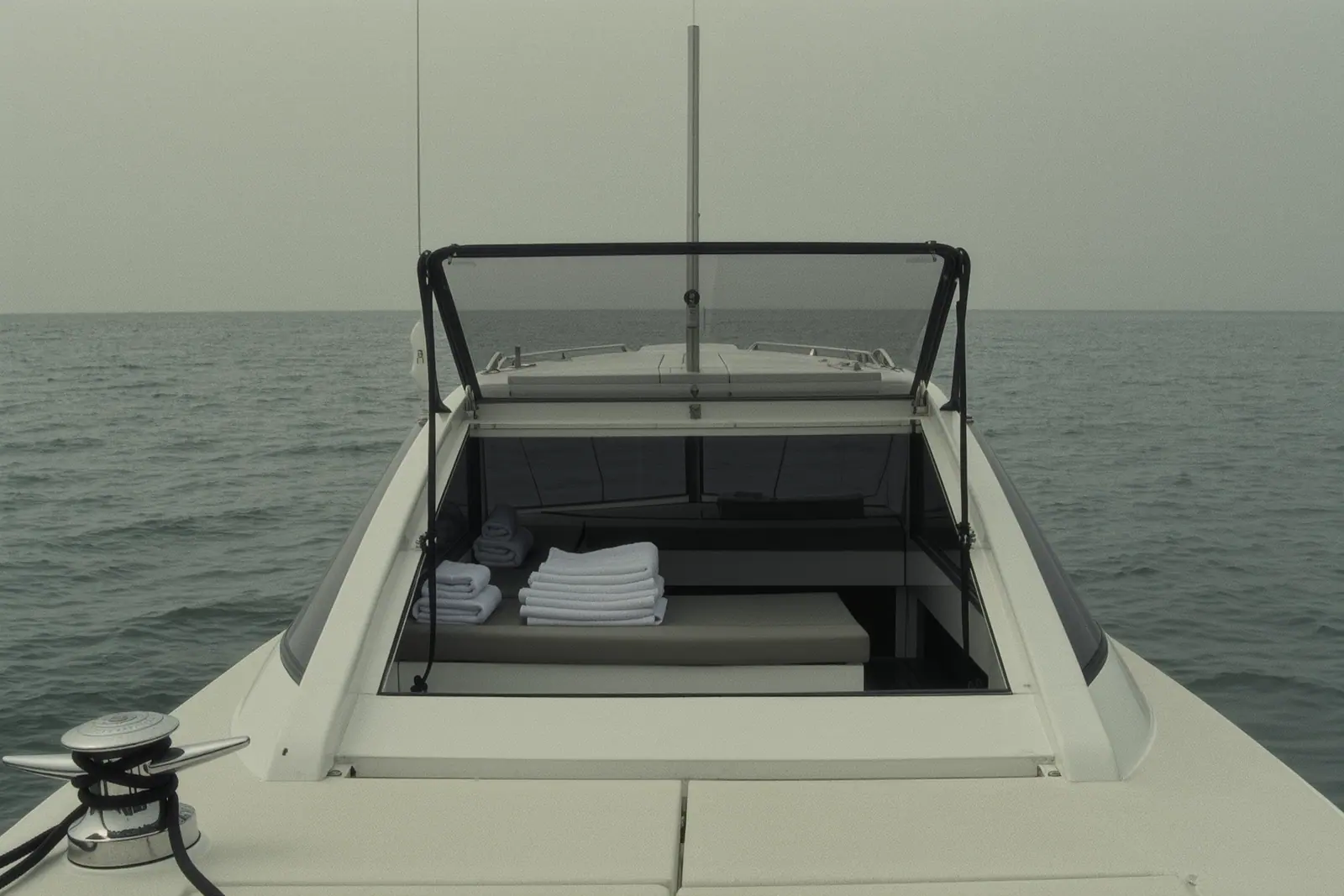 The empty aft deck of a motor yacht with folded towels stacked on the bench seat and the boarding gate open, a stainless cleat and coiled line in the foreground.